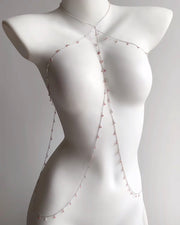 A delicate silver-toned body chain with small pink beads, displayed on a white female mannequin torso against a light gray background.