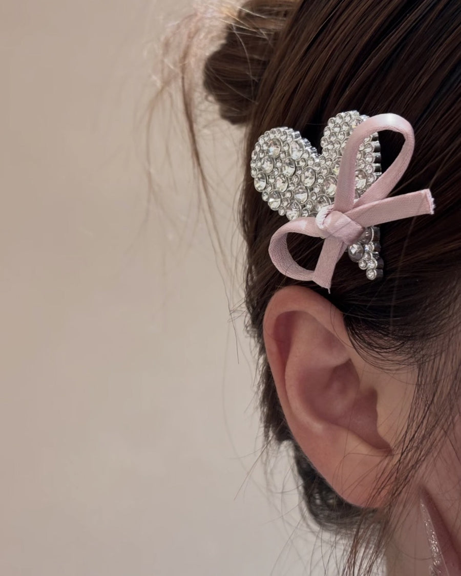 Rosette Kiss rhinestone heart hair clip with a pink satin bow, worn above the ear with a messy bun