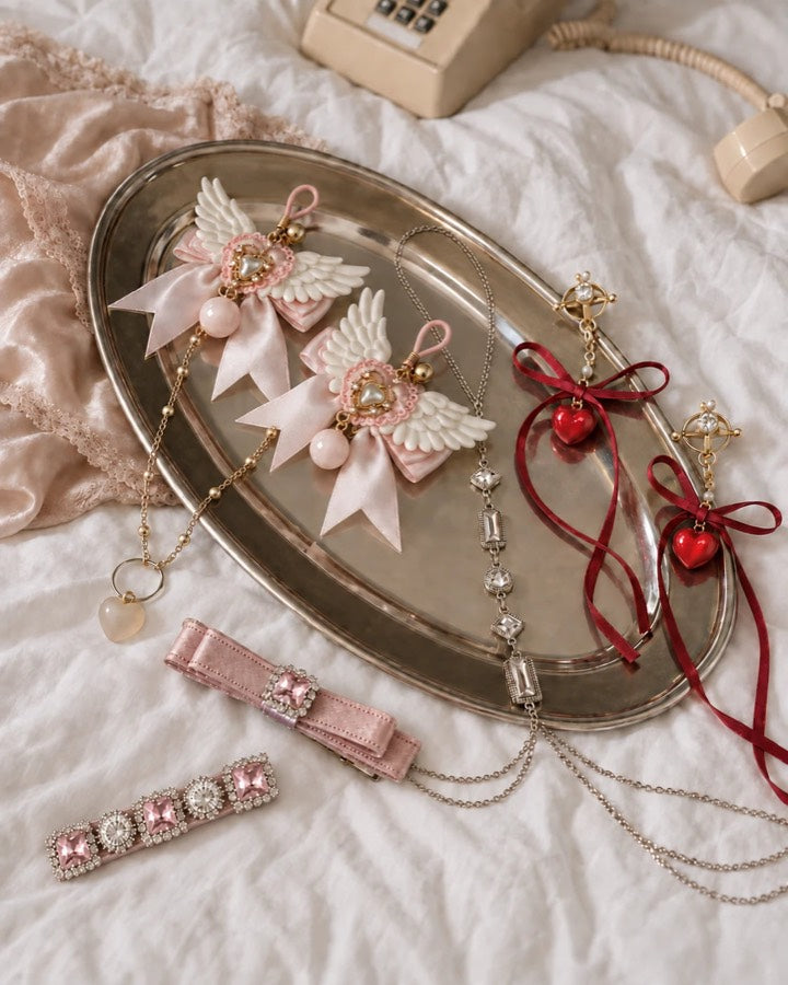 Angel-wing bows, red heart charms and crystal chains laid on a silver tray
